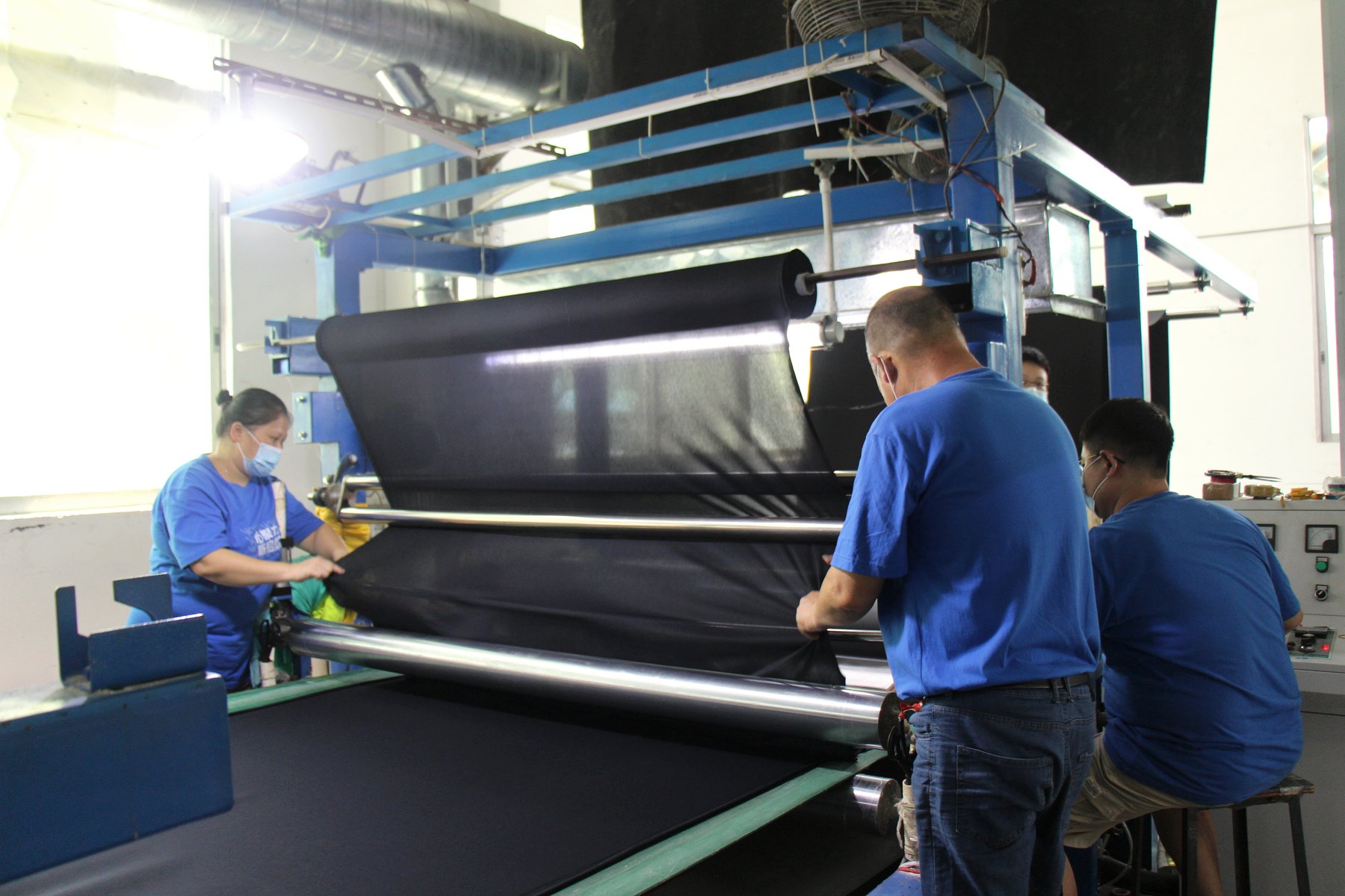 Workers operating neoprene lamination equipment inside the factory